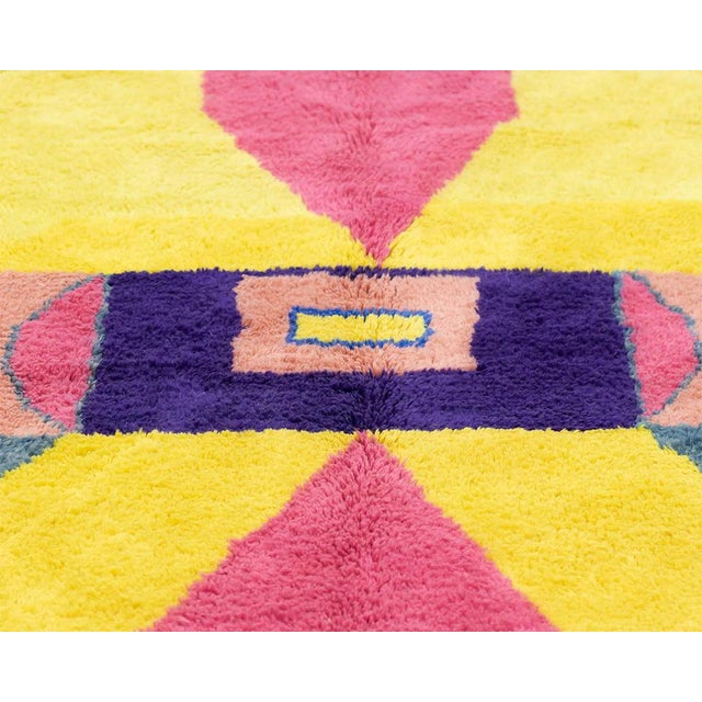 A burst of color, arranged with mirror-like precision. Bold triangles in canary yellow and fuchsia pink converge toward a...