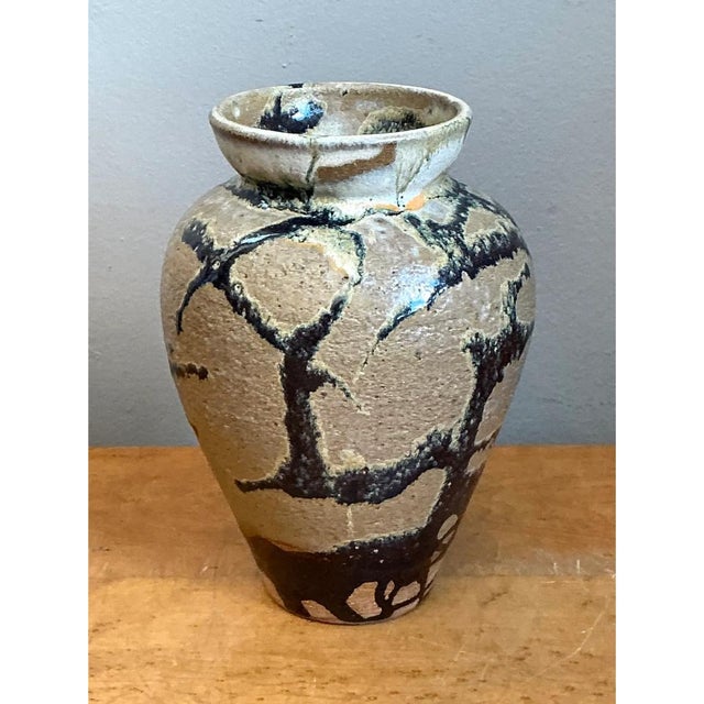 This vintage stoneware vase is a rugged, deeply tactile object, its broad, shouldered body tapering gracefully to a narrow...