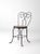 A vintage ice cream parlor chair in black metal, featuring a wide back with the classic “spectacle” design and a wood...
