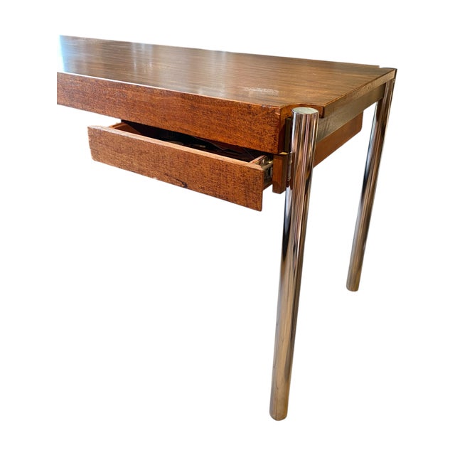 A modern wood and steel desk with a slim top supported bu tubular chrome legs. One drawer. The top is laminate and in...
