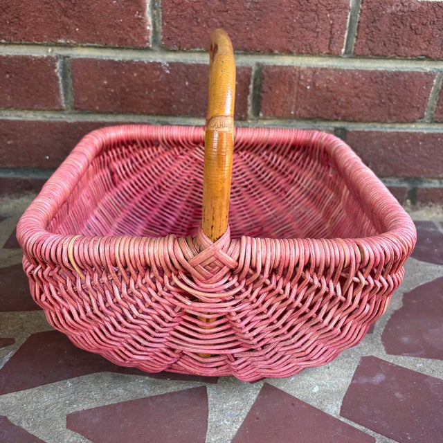 This vintage wicker gathering basket is painted a soft dusty rose and woven in a square shape with a bamboo cane handle....