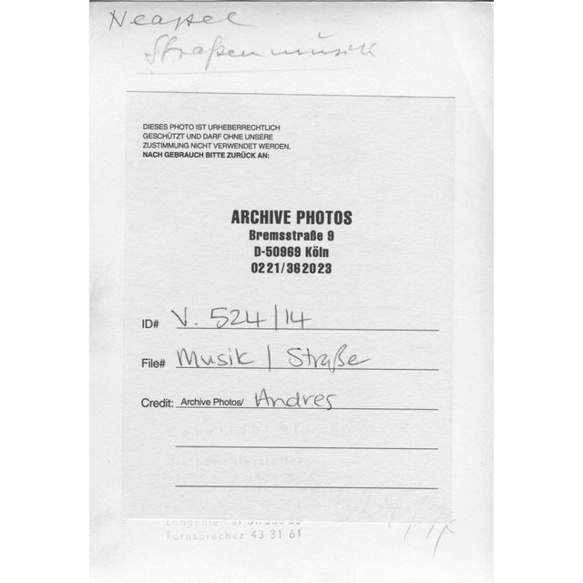 This photograph, taken in Naples in 1954, depicts a group of street musicians performing in what appears to be an urban...