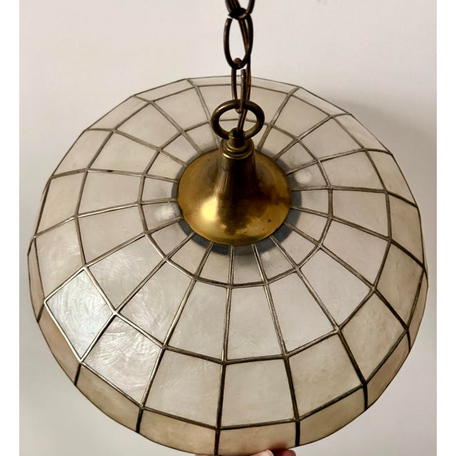 Here is a beautiful vintage capiz shell pendant light, likely dating to the 1960s–1970s. It features a saucer-shaped shade...
