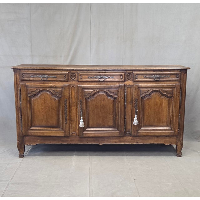A gorgeous and functional antique early 1800s French oak buffet with three doors and three drawers that sits on curved...