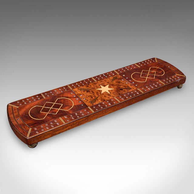 This is an antique Cribbage board. An English, inlaid game scoreboard with pin storage in mahogany and bird's eye maple,...