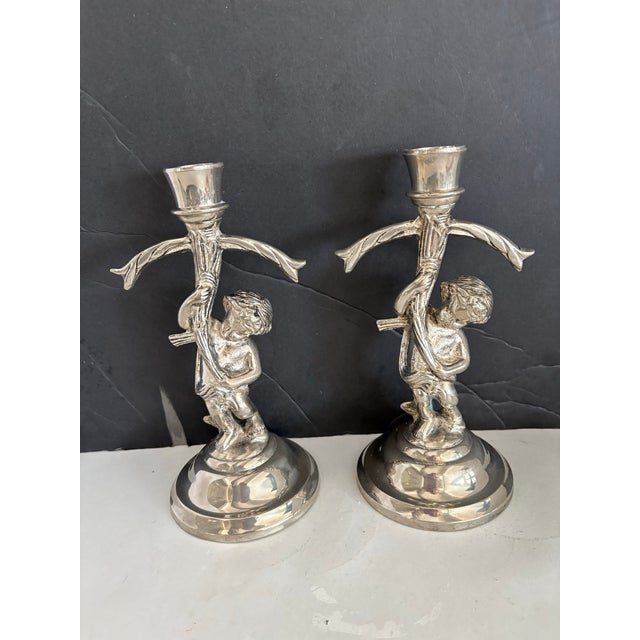 A charming pair of antique silver-plated figural candlesticks, each sculpted as a cherub child entwined with a...
