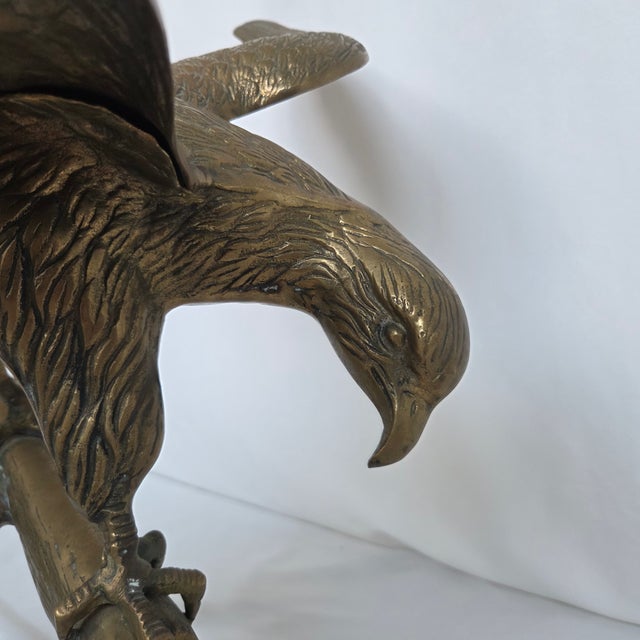 This substantial vintage brass eagle sculpture depicts a dramatic bird of prey perched on a naturalistic tree branch with...