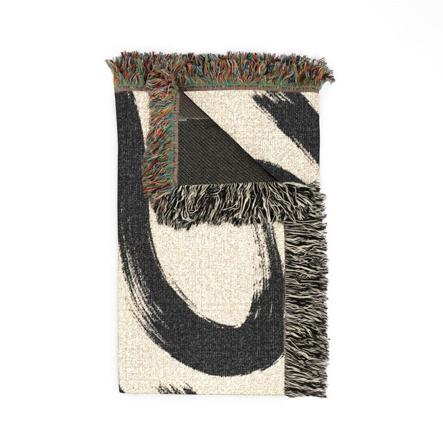 This black and cream abstract woven throw blanket features sweeping brushstroke shapes, textured cotton construction, and...