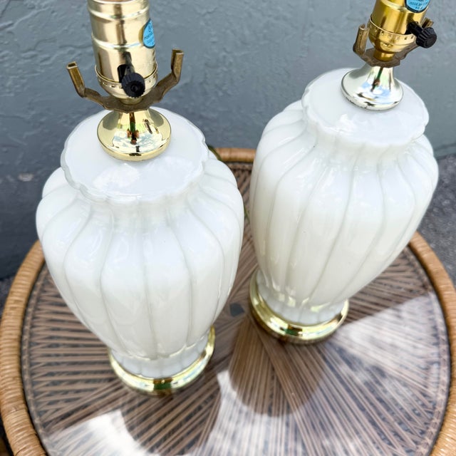 A glamorous pair of Hollywood Regency table lamps featuring sculptural white milk glass bodies with elegant scalloped...