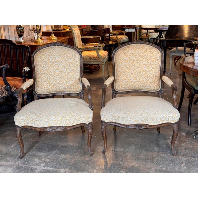 Pair of 19th century French armchairs with carved walnut toned frames. The arched backs are topped with carved floral...