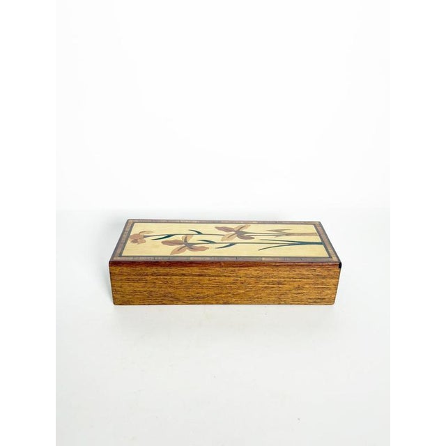 Decorative rectangular wooden box featuring an elegant marquetry decoration on the lid. The composition depicts stylized...