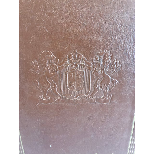 A large vintage leather scrapbook album featuring an embossed crest, gold tooling, and a traditional rope-tie binding. The...