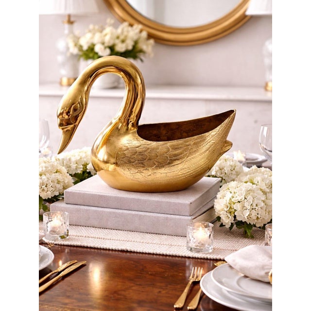 A bold Hollywood Regency brass swan planter featuring a gracefully arched neck, detailed featherwork, and a luminous...