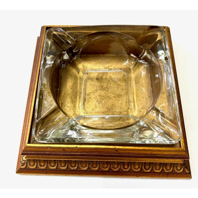 A striking vintage pressed-glass ashtray set into a stepped gilt-finished wooden base, combining sculptural glass with...