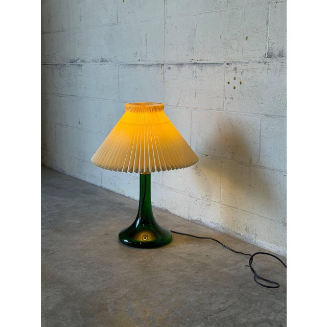 This charming table lamp features a graceful green glass base topped with a classic pleated shade. It delivers warm...