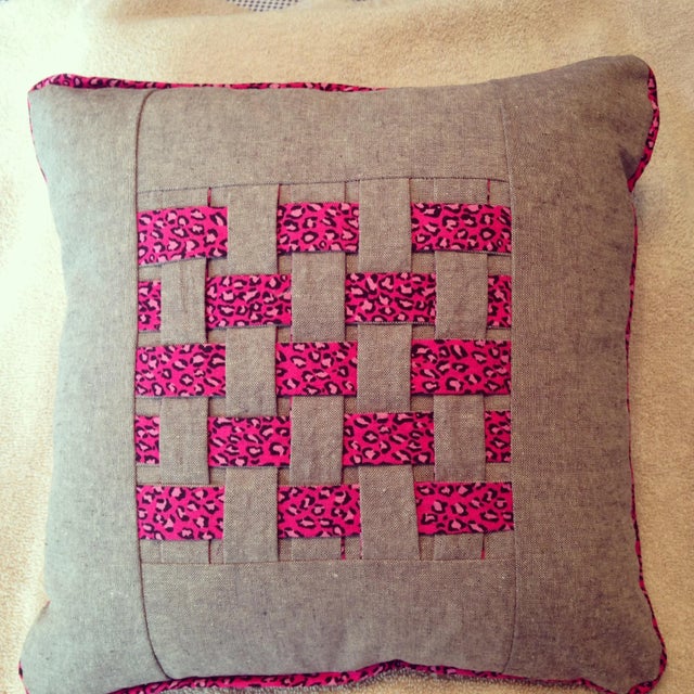 Pretty grey throw pillow with a pink leopard print criss-cross design measuring approx. 12 inches X 12 inches X 4 inches....