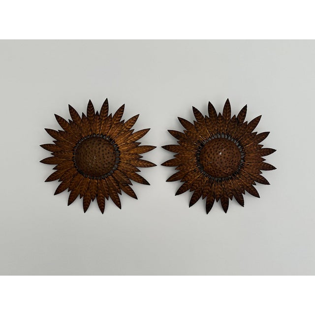 A pair of vintage Spanish wall lamps in aged bronze/copper metal. The sunburst design features multiple concentric, petal...