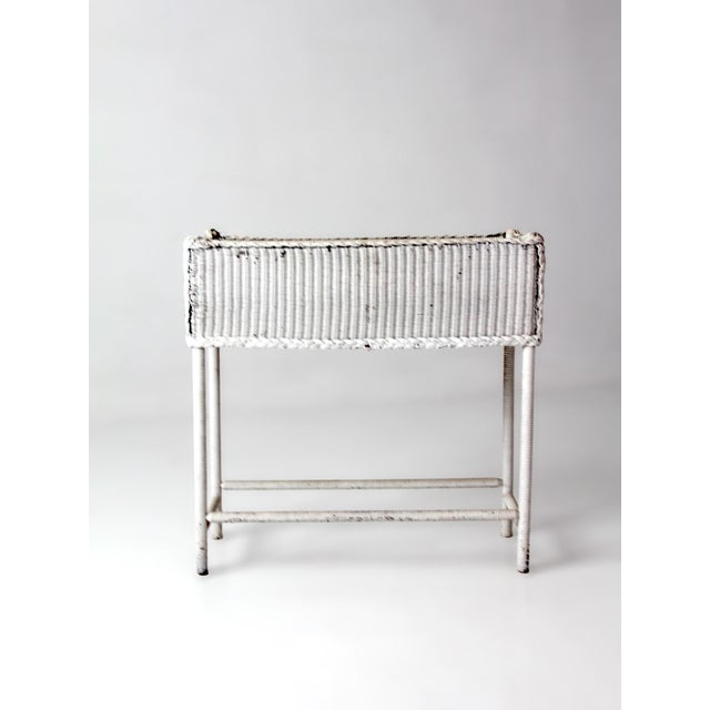 This early 20th-century wicker plant stand features a long rectangular form, braided trim detailing, and a removable...