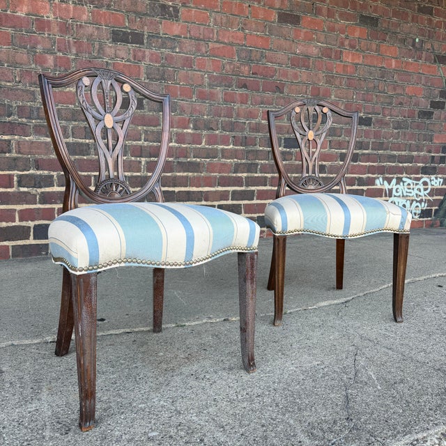 This is a pair of Heppelwhite Style dining side chairs. They feature an intricately carved wooden backrest with blue and...