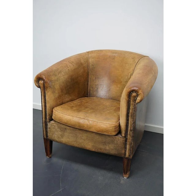 This vintage club chair is upholstered with cognac-colored leather and features metal rivets and wooden legs.