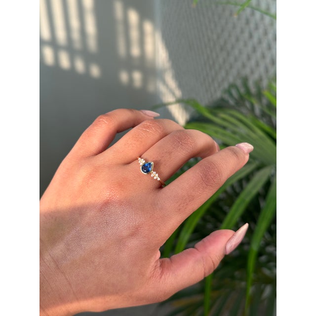 This cluster engagement ring features a 0.67 carat of pear-shaped blue sapphire set in 14K yellow gold. The sapphire...