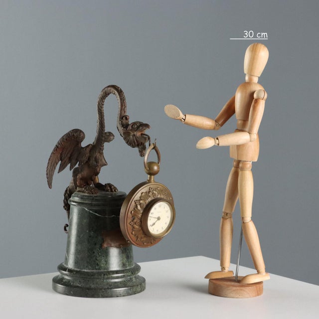 Bronze clock with embossed plant motifs and a dial with Arabic numerals. The clock is supported by a bronze griffin...