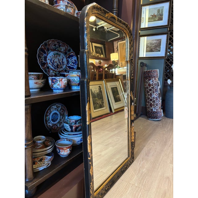 A striking vintage black lacquer Chinoiserie mirror featuring hand-painted gilt decoration inspired by traditional East...