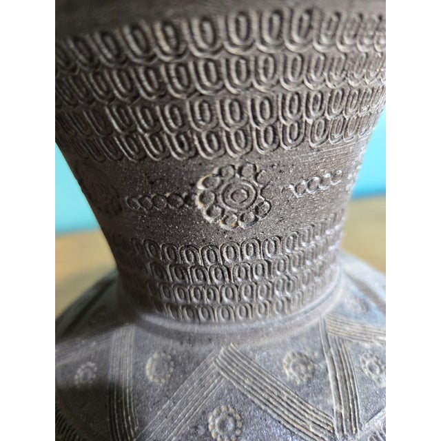 This is a handmade clay vessel that has a wide flaring rim and bulbous body and features densely stamped geometric...