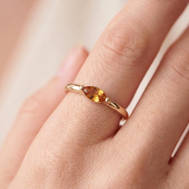 A radiant, minimalist solitaire featuring a golden-hued marquise-cut citrine set in an east-west orientation, secured by a...