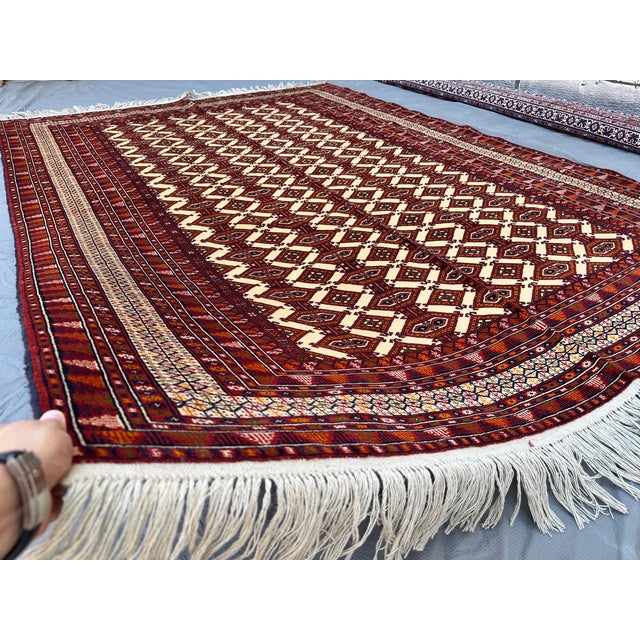 This striking Turkmen Bokhara rug presents a diagonal zigzag lattice of elongated diamond compartments in warm rust and...