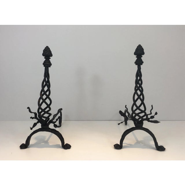 This pair of wrought iron andirons is made of a twisted central part with ribbons on the base and a large finial on top....