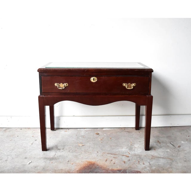 A vintage dark wood display table with a drawer front, glass top, and brass hardware. The display drawer and the base are...