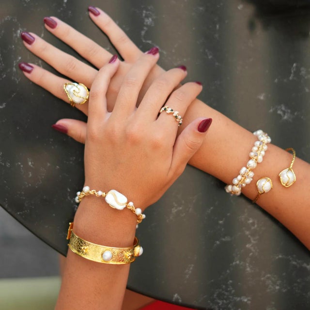 The Cleopatra Twisted Design Pearl & Gold Cuff Bracelet is a beautifully crafted 24k gold-plated brass cuff featuring a...