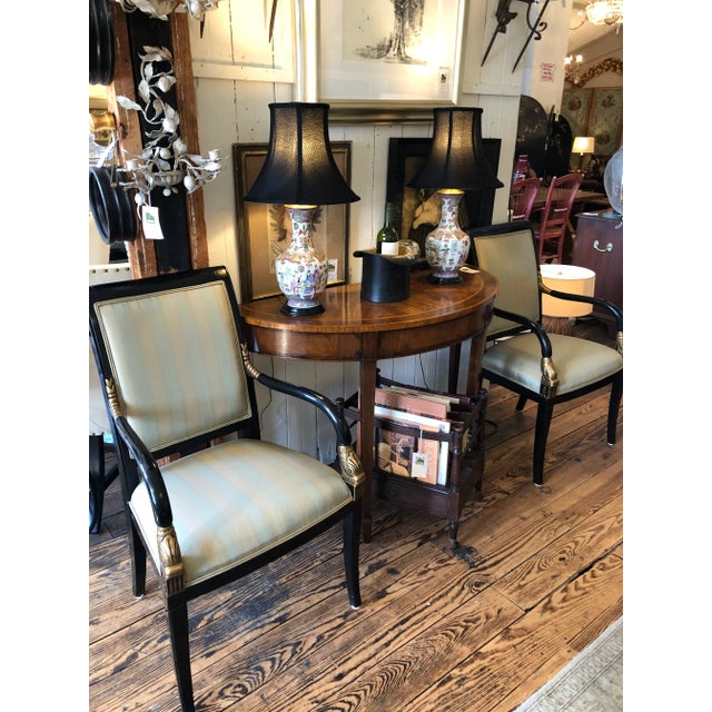 Handsome pair of Regency style armchairs having black frames with gilded dolphin motif decoration on the arms and neutral...