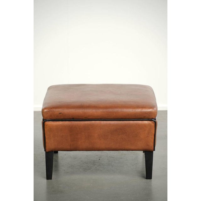 This sheepskin ottoman is versatile, features a warm cognac color, and is finished with black piping. A footstool, also...