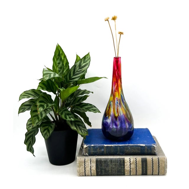 A stunning hand-blown art glass vase with a dynamic swirl of colors blending from deep violet to amber, golden yellow, and...