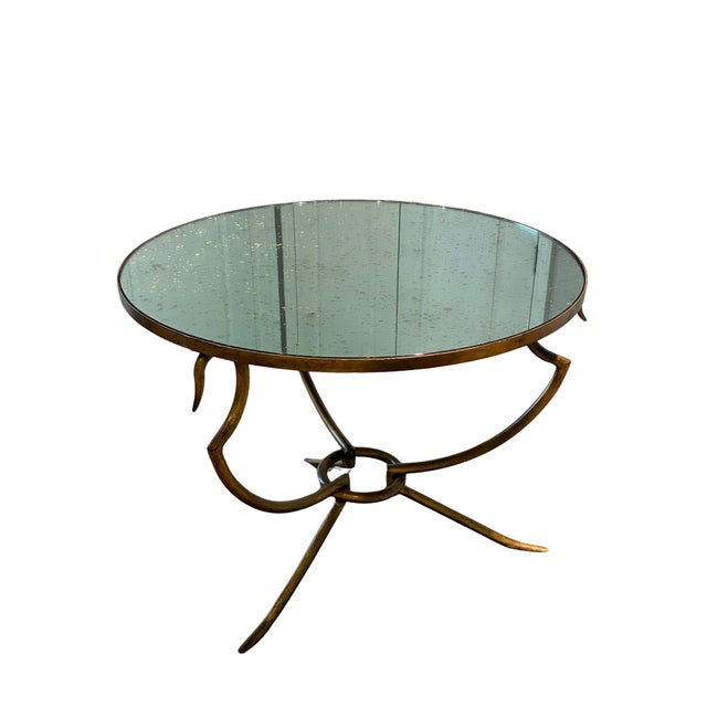 An elegant and sculptural round accent table by Baker Furniture, featuring a beautifully antiqued mirrored top supported...