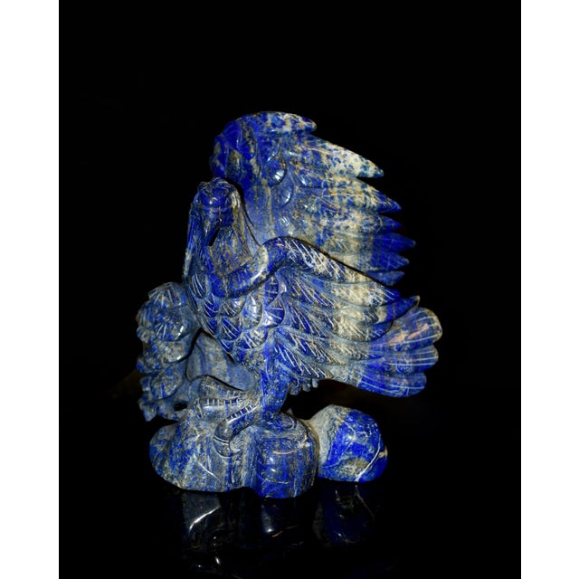 A striking hand-carved sculpture of an eagle poised upon a pine tree, rendered from natural lapis lazuli of rich,...