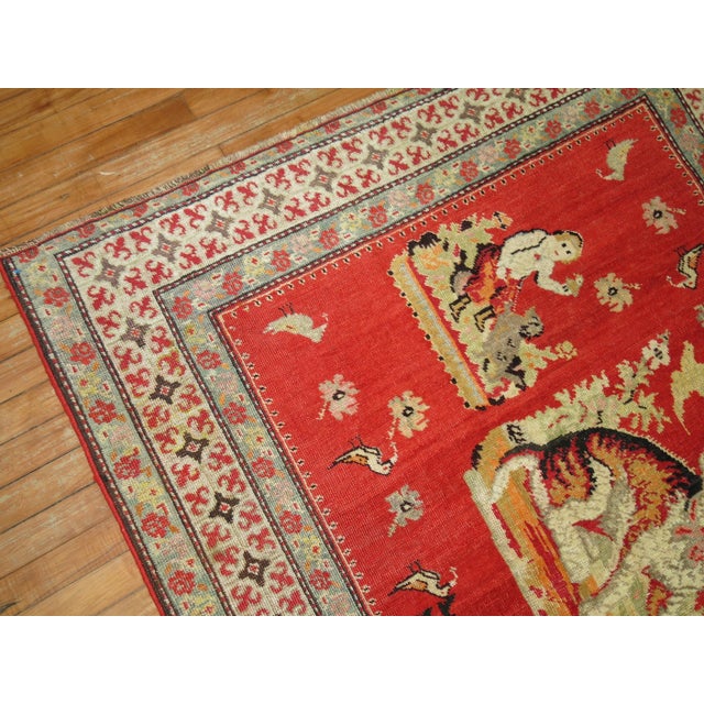 A pictorial rug depicting a dog floating around different humans, animals, and figures on a red ground. 3'9'' x 6'2''