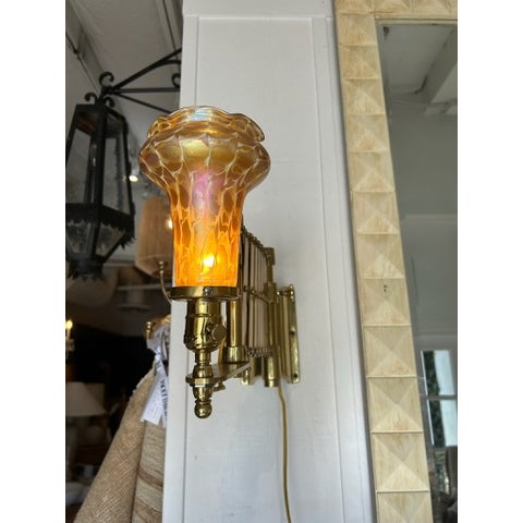 Vintage brass scissor wall lamp featuring an adjustable accordion arm and a striking iridescent art glass shade. The...
