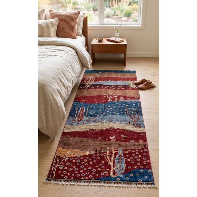 A hand-knotted runner in the Persian Gabbeh style, woven as a landscape in bands of madder red, camel brown, indigo and...