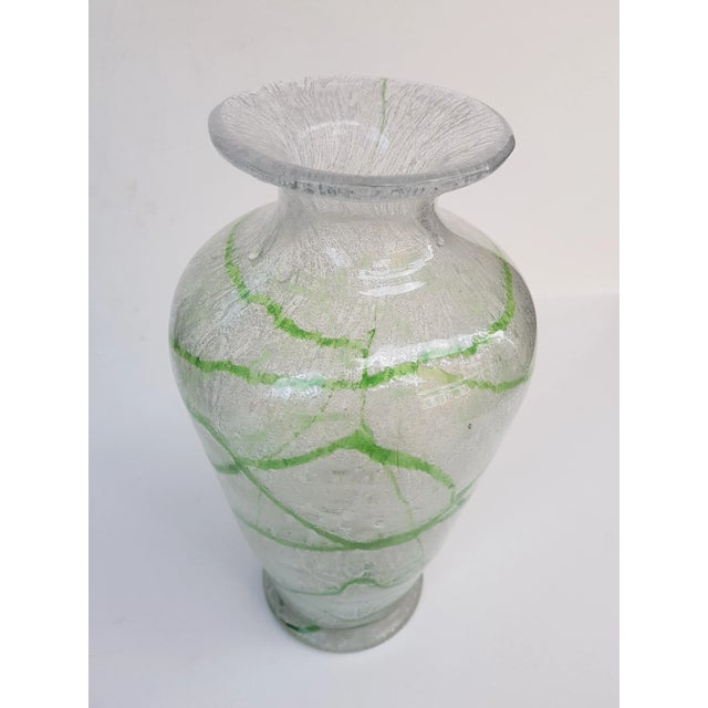 Large foam glass vase made of colorless glass with irregularly braided green thread decoration and white powder between...