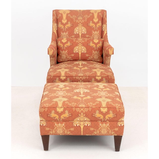 Baker Floral and Animal Upholstered Wingback Armchair and Ottoman, in burnt orange and golden accents, label to underside....