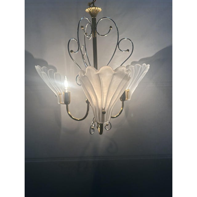Three-light chandelier in brass and silver plating. Shell-shaped glass in satin white. Up to 250V (Europe/UK Standard).The...