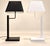 Each lamp rests on a flat, square, lacquered metal base, extended by a rectangular vertical stem and a right-angled arm...