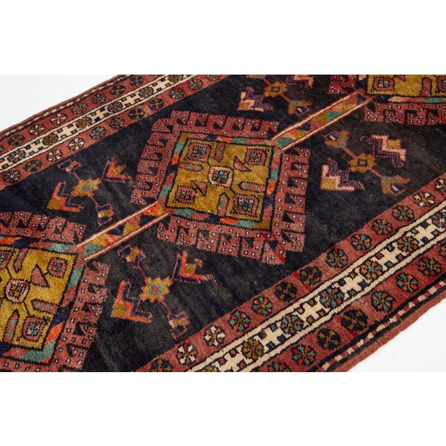 This Vintage Persian Heriz rug is hand-knotted with a dark blue field, a rust-red frame, and multicolor accents in an all-...