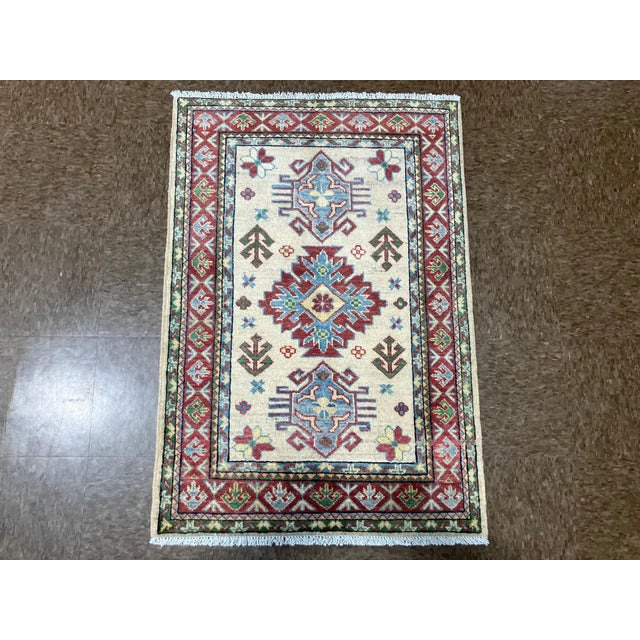 Hand-knotted Pakistani Kazak wool rug featuring an ivory field with a central geometric medallion and stylized tribal...