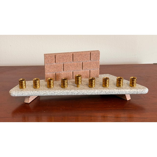 This well-designed menorah pairs a grey and rose cultured stone base with nine turned brass candle cups, the back panel...