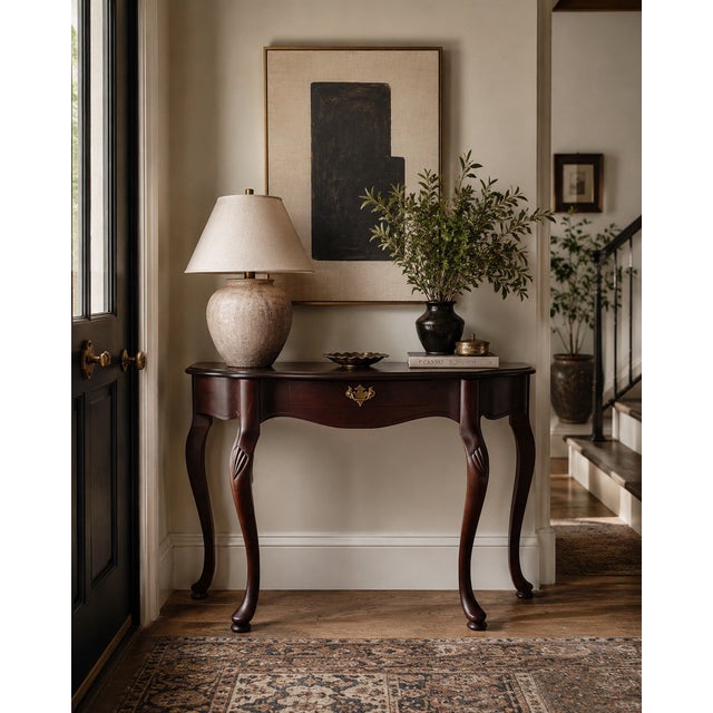 This vintage mahogany demi-lune entryway table features a graceful serpentine front, long cabriole legs, and carved shell...