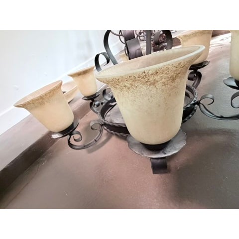 A charming six-arm wrought iron chandelier with frosted cream glass bell shades and twisted arm detailing. Dark iron...